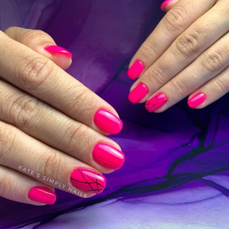 A closeup of a woman's fingernails with neon pink nails that has a little twist of black lines and curves
