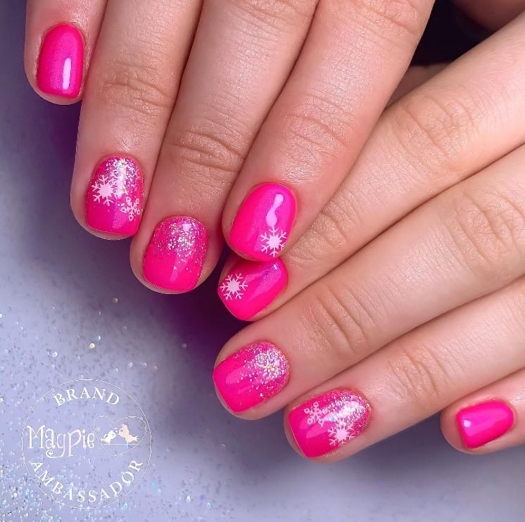 A closeup of a woman's fingernails with neon pink nails that has glitter design and a super cute snowflake stickers