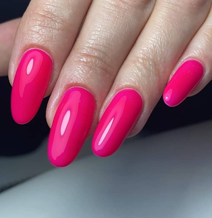 A closeup of a woman's fingernail with medium-length oval neon pink almond nails that has made better with high gloss