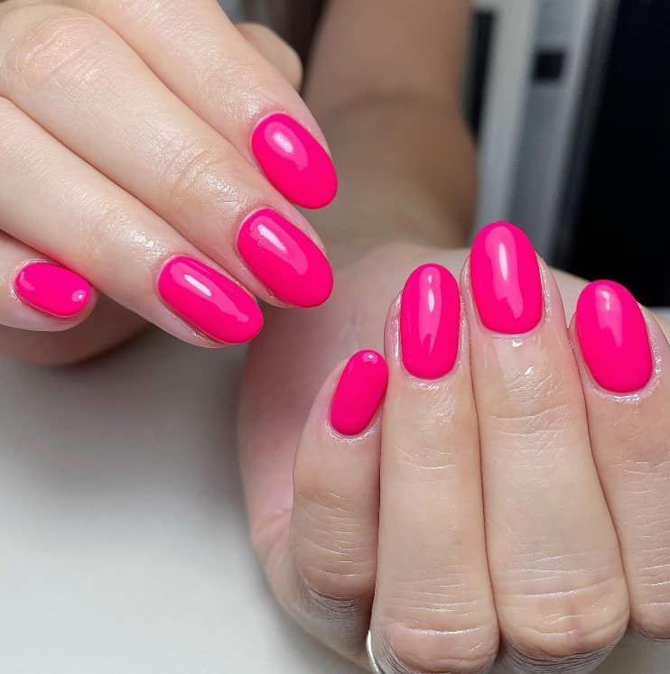 A closeup of a woman's fingernails with a glossy neon pink nail polish 