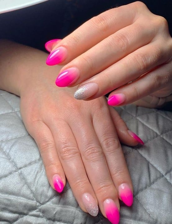 A woman's fingernails with neon pink ombre that has silver glitters nail tips on select nails 