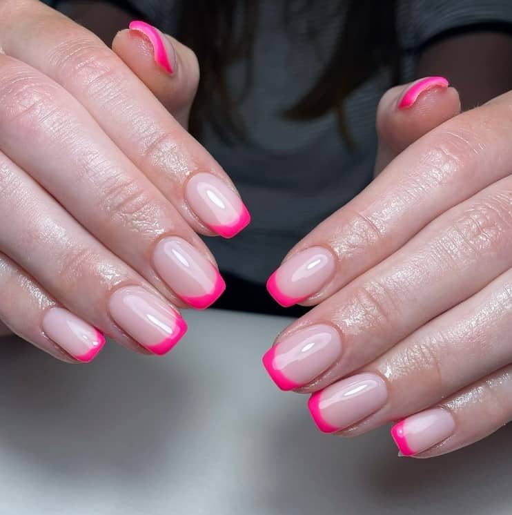 A closeup of a woman's fingernails with a glossy nude nail polish that has thin neon pink tips