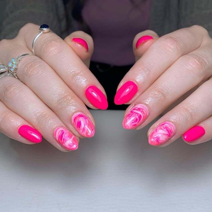 A closeup of a woman's fingernails with a hot pink nail polish base that has pink and white marbling on your accent nails