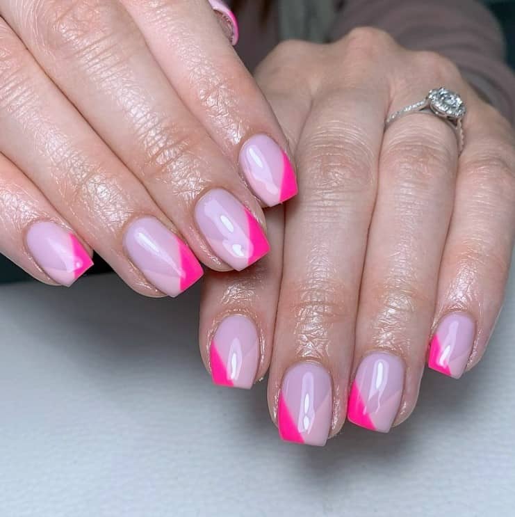 A closeup of a woman's fingernails with a glossy light pink nail polish base that has neon pink and pale pink as V- cut French tips
