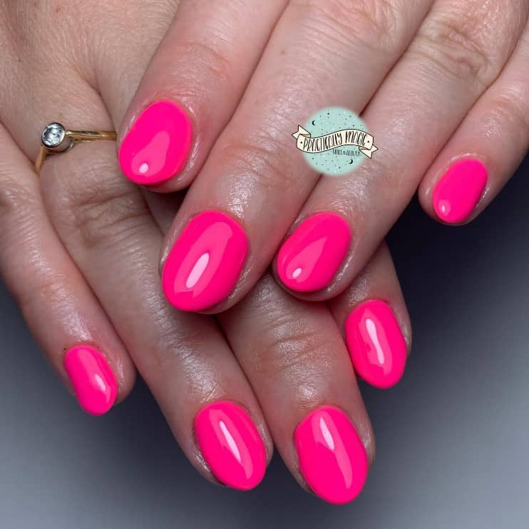 A closeup of a woman's round fingernails with bright neon pink nail polish