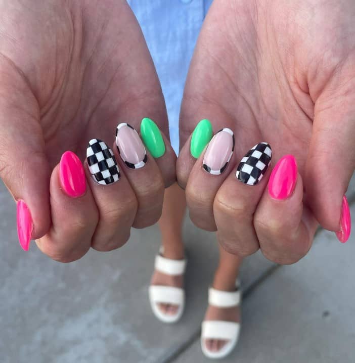 A woman's fingernails with neon pink, bright green, and silky mocha nails that has checkered patterns on select nails in a racing-inspired nails