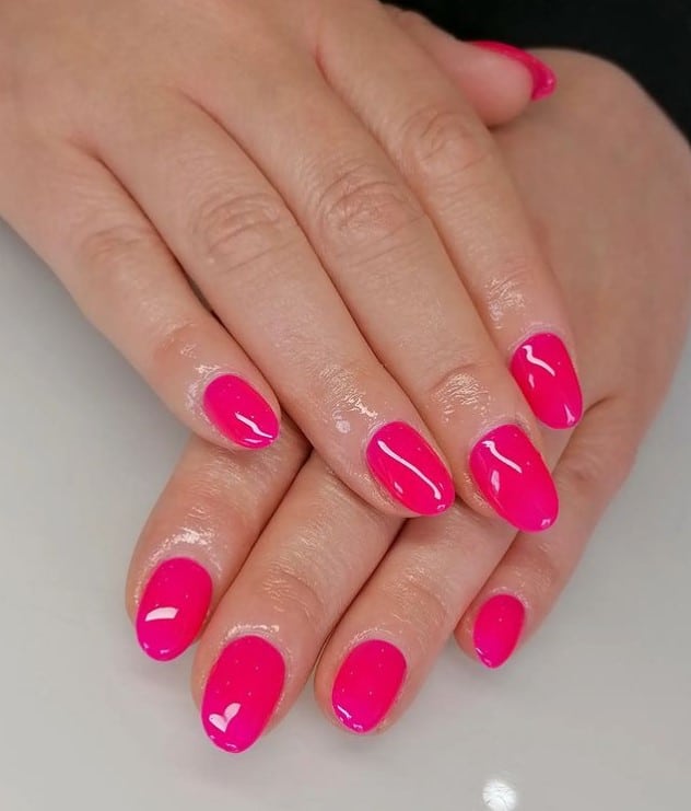 A woman's fingernails with a glossy neon pink nail polish
