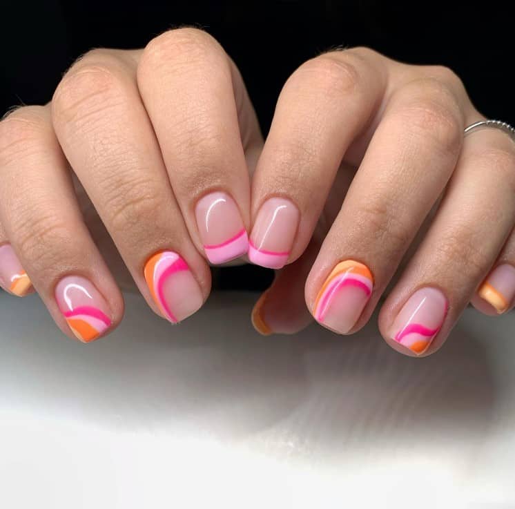 A closeup of a woman's fingernails with a nude nail polish that has French tips by using two shades of pink and orange and swirl designs along the tips