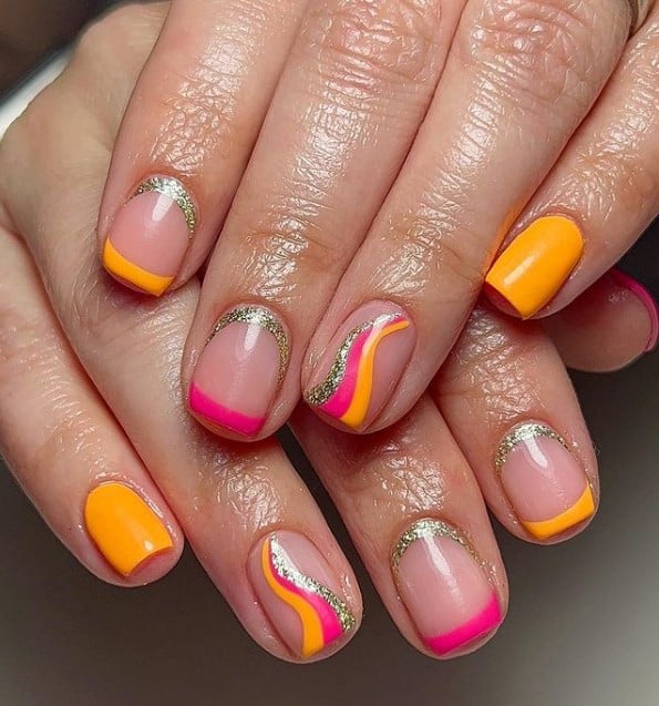 A closeup of a woman's fingernails with a combination of nude and orange nail polish that has pink and orange French tips, silver glitter cuticle cuffs and swirls