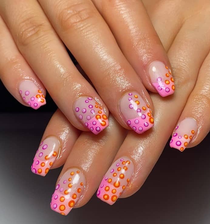 A closeup of a woman's fingernails with a nude nail polish that has ombré pink French nails with pink-and-orange bubble nail art