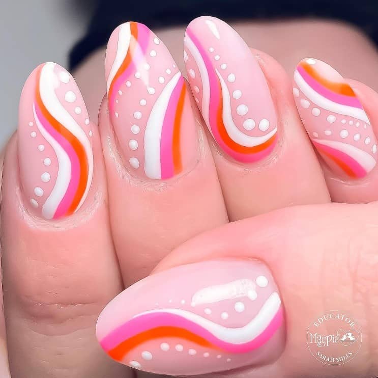 A closeup of a woman's fingernails with a nude nail polish base that has white dots, white, pink and orange swirls