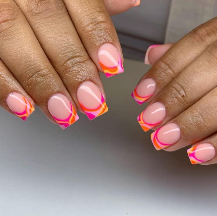 A woman's fingernails with a nude nail polish base that has orange and pink wavy French tips 