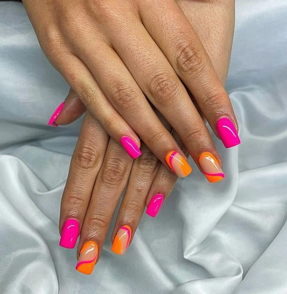 A woman's fingernails with a combination of pink and orange nail polish that has swirls designs