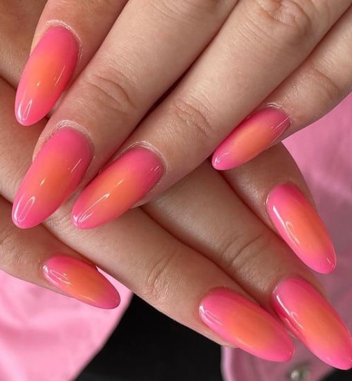 A closeup of a woman's oval-shaped fingernails with ombré pink-and-orange nail polish 