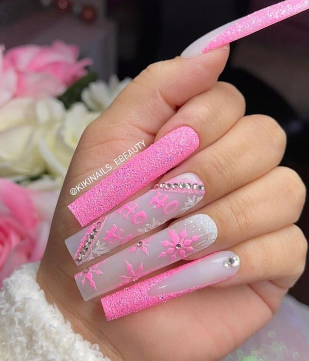 A closeup of a woman's fingernails with a combination of white and pink neon nail polish that has glitter accents, rhinestones, and wintry nail art