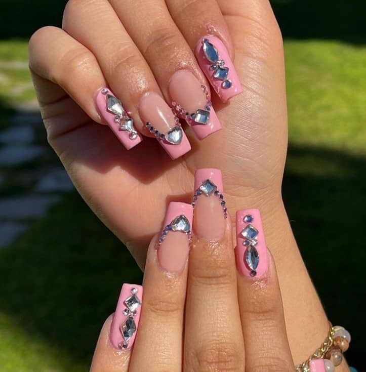 A woman's fingernails with a nude and pink nail polish that has different rhinestones and pink French-tip accent nails