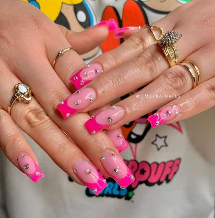A closeup of a woman's fingernails with a pink nail polish base that has hot pink nail tips and rhinestones to each nail in a polka-dot pattern