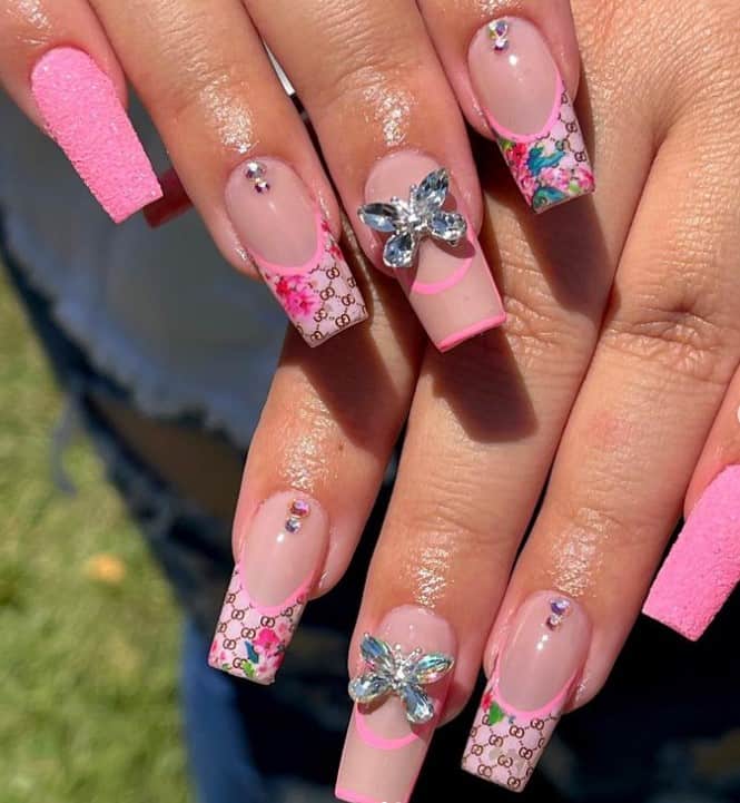 A closeup of a woman's fingernails with a combination of nude and pink nail polish that has butterfly rhinestone and sugary pink nails 