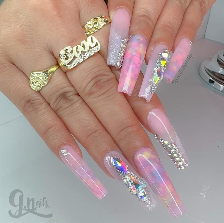 A woman's fingernails with a clear and pink nail polish that has two rhinestone-embellished nails 