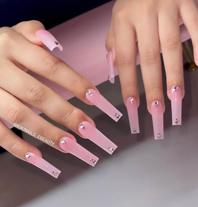 A closeup of a woman's fingernails with pink nail polish that has two little stones near the cuticles and tips