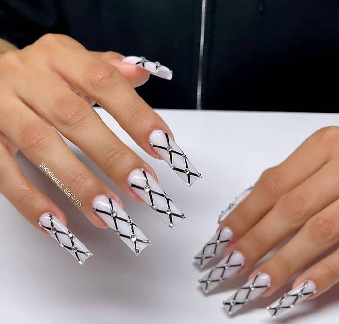 A woman's fingernails with a white nail polish base that has rhinestones on the edges of black criss-cross design
