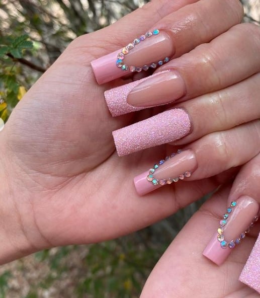 A closeup of a woman's fingernails with a mix of a nude and pink nail polish that has little gems