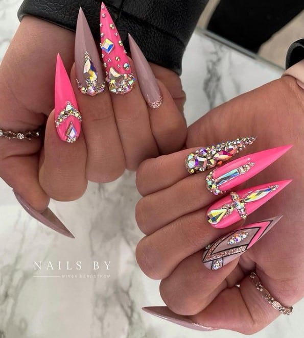 A closeup of a woman's fingernails with a hot pink and brown nail polish that has different types of rhinestones 