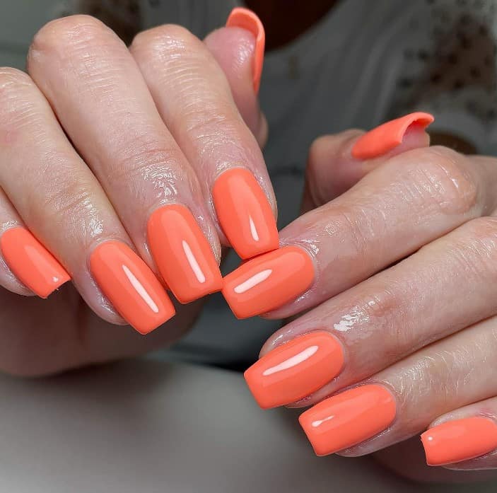 woman's squared fingernails with bright coral nail polish