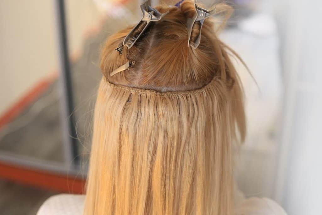 A photo of a woman with long blonde hair with sew in hair extension in a salon.