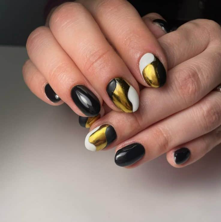 A closeup of a woman's fingernails with a black nail polish that has white and gold nail swirls