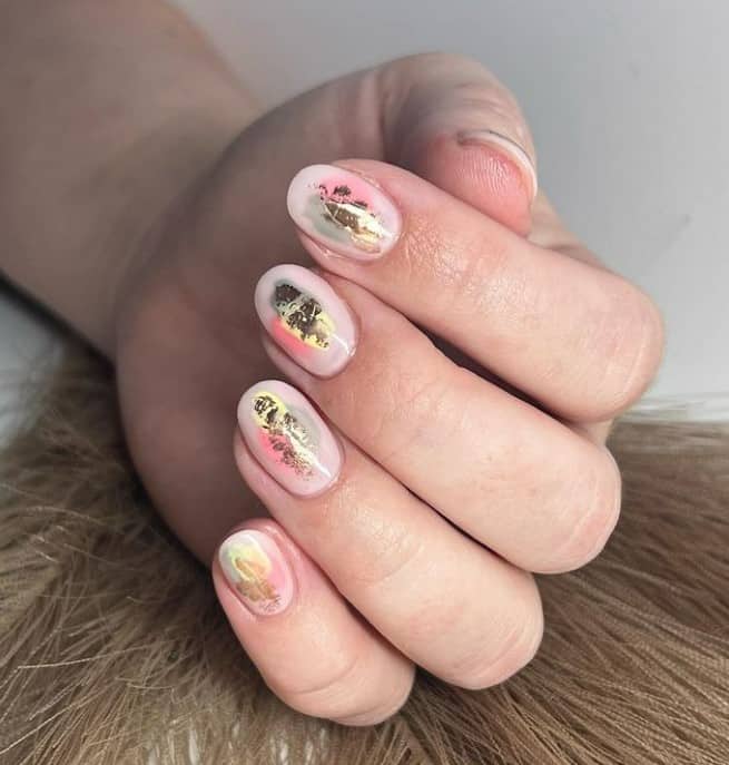 A woman's fingernails with pale peach nails that has metallic gold flakes and pink and gray splotches