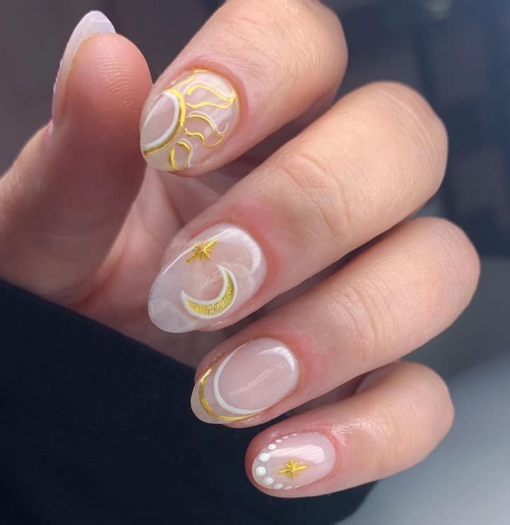 A closeup of a woman's fingernails with off-white nails that has sun, moon, and stars nail designs in white and gold nail polish