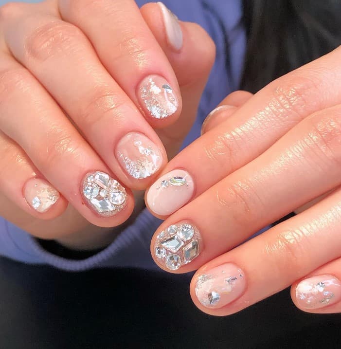 A closeup of a woman's fingernails with a nude nail polish that has varying amounts of rhinestones