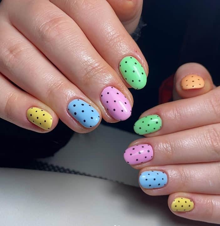 A closeup of a woman's fingernails with yellow, blue, pink, green, and orange nail polish that has black dots