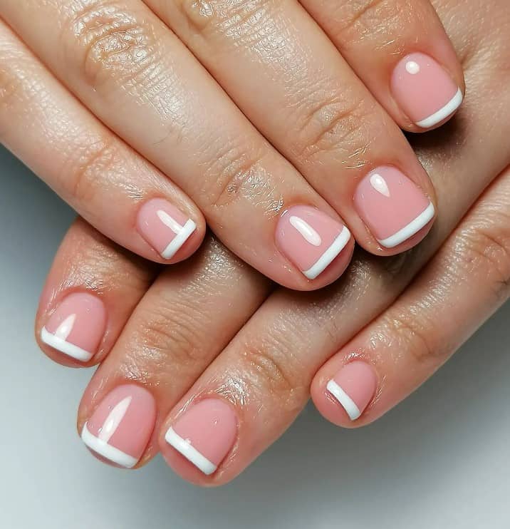 A closeup of a woman's fingernails with a glossy pale pink nail polish that has solid white tips