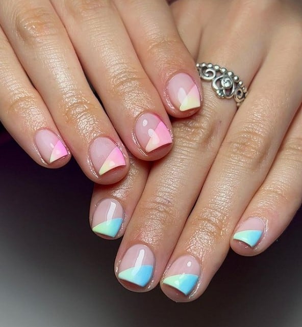 A closeup of a woman's fingernails with a nude nail polish that has pink-and-yellow ombré for the tips on one hand and a green-and-blue ombré on the other