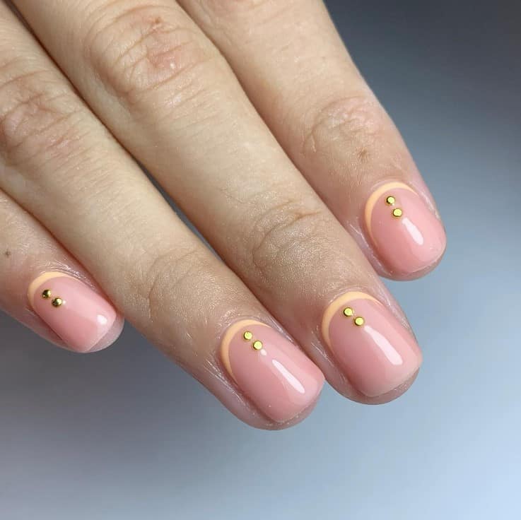 A closeup of a woman's fingernails with pale pink nails that has peach-colored cuticle cuffs and two peach gems above the cuticles