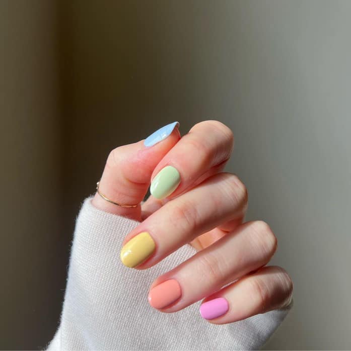 A woman's fingernails with combination of soft blue, green, yellow, orange, and pink nail polish 