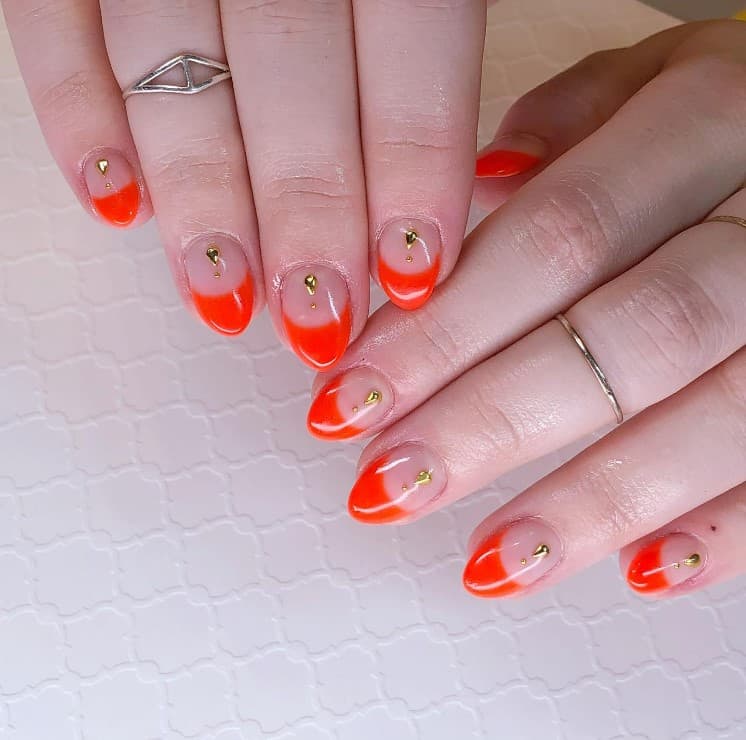 A closeup of a woman's fingernails with a nude nail polish base that has thick orange bands on nail tips 