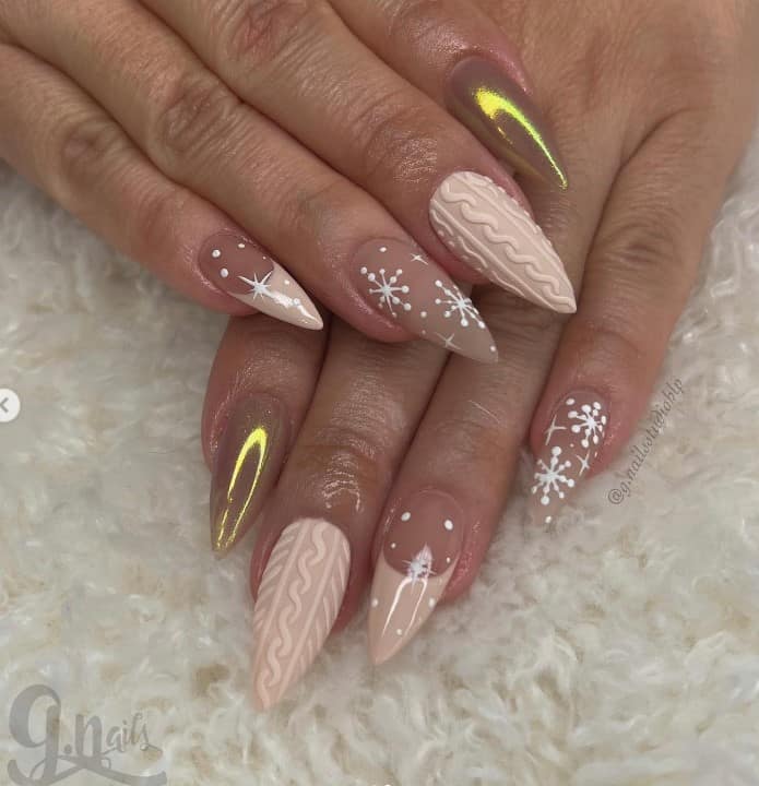 A closeup of a woman's short stiletto fingernails with a pale nude nail polish that has glazed monochromatic nails, knitted-sweater nail art, and white snowflakes