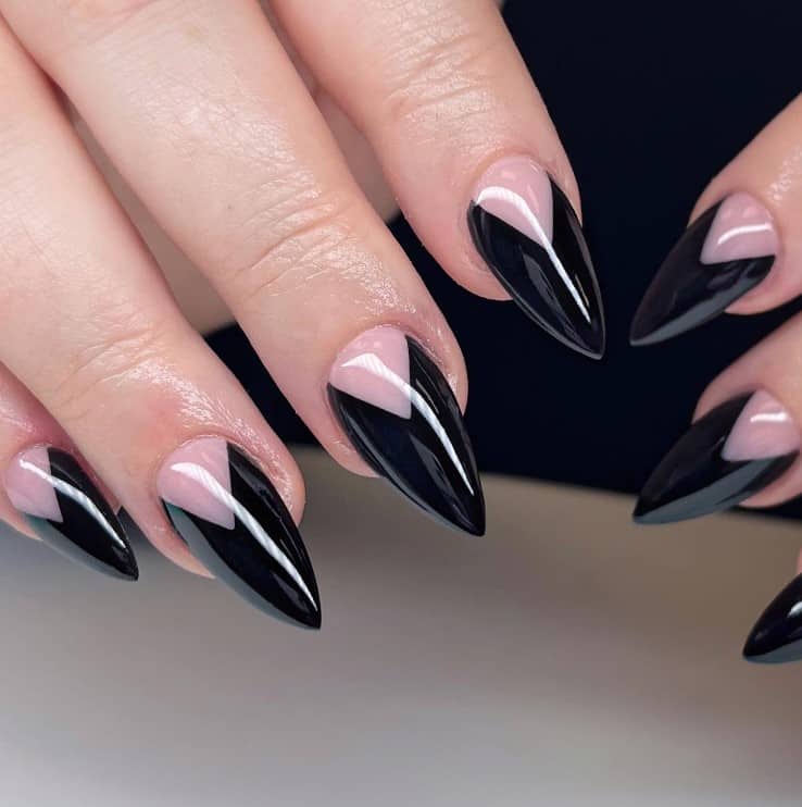 A closeup of a woman's short stiletto fingernails with a nude nail polish that has thick V-tips in black polish