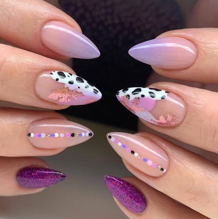 A closeup of a woman's fingernails with a nude nail polish base and purple glitter nail polish that has ombré, cow print, glitter, and polka dots  