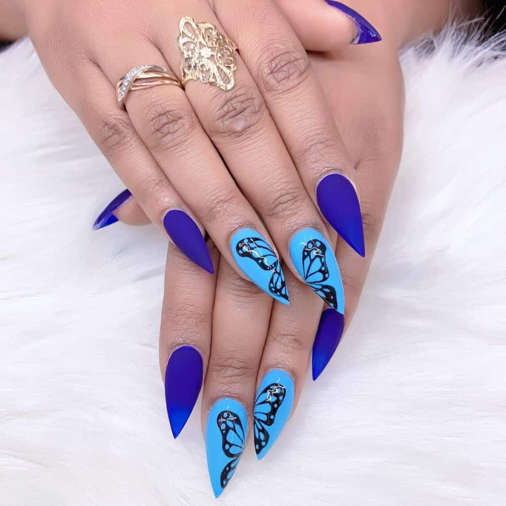 A closeup of a woman's fingernails with a matte blue and glossy blue nail polish that has a butterfly to the accent nails