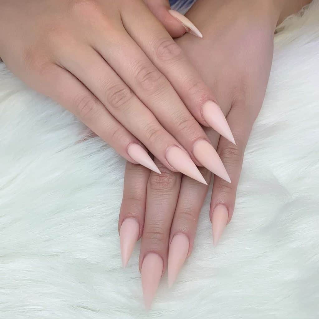 A woman's short stiletto fingernails with a nude nail polish in a a matte finish