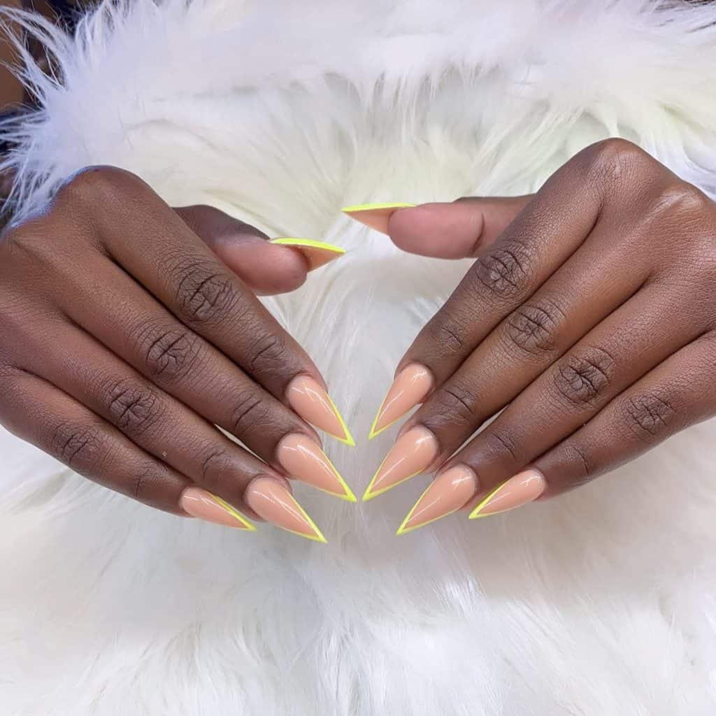 A woman's pointy tips stiletto fingernails with a glossy nude nail polish that has bright yellow nail tips