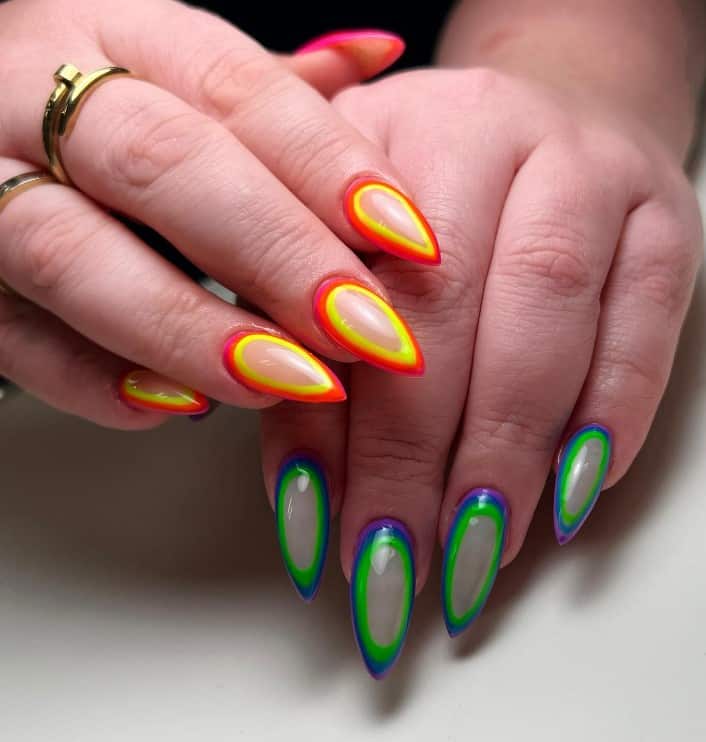 A closeup of a woman's stiletto fingernails with orbit nail art that has orange-and-yellow and blue-and-green outlines