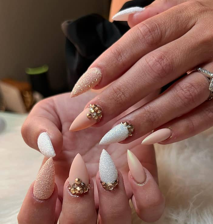 A woman's fingernails with a nude and white nail polish that has glitter and rhinestones on select nails 