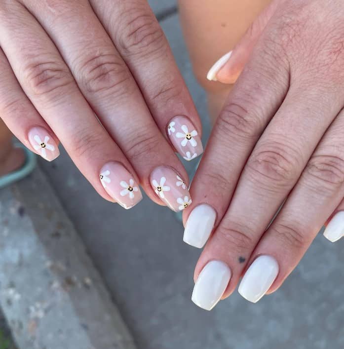 A woman's fingernails with a white nail polish on the other hand and nude nails on the other that has smiley flowers on the nude nails 
