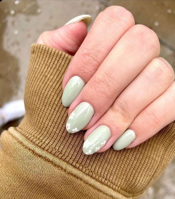 A closeup of a woman's fingernails with a pistachio green shade that has tiny flowers to the tips