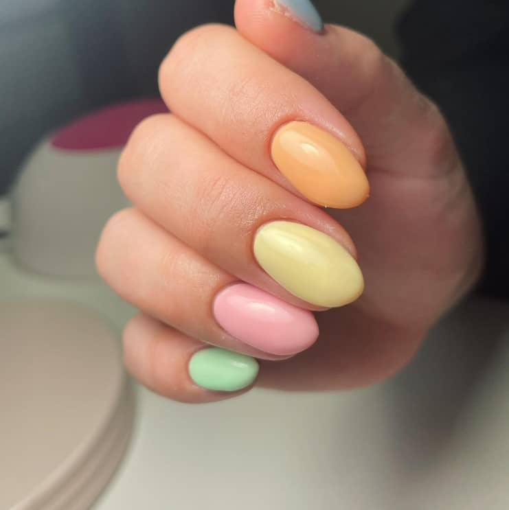 A closeup of a woman's fingernails with a multicolored pastel nail polish 